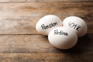 Eggs with words PENSION, RETIRE and 401k on wooden background. Space for text