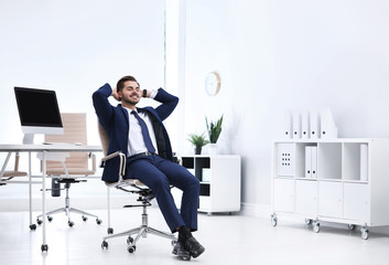 Young businessman sitting on office chair at workplace, space for text