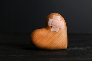 Wooden heart with adhesive plasters in darkness on table