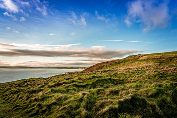 Scenic view of sea by green hill against blue sky during sunset