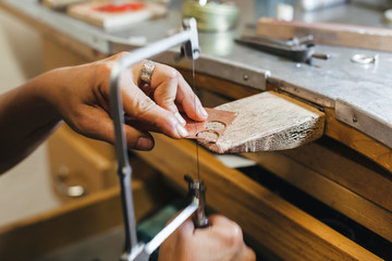 Cropped hands of female artisan using handsaw while working on table in workshop