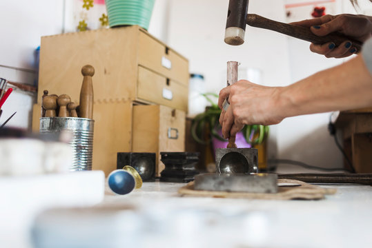 Cropped hands of female entrepreneur hammering dapping punch on doming block in workshop - Powered by Adobe