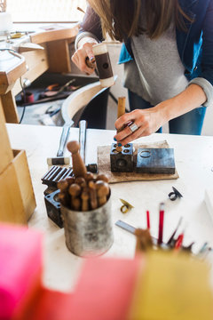 Midsection of female jeweller hammering dapping punch on doming block in workshop