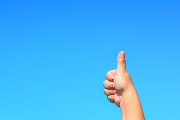 A male hand shows a thumbs up symbol sign isolated against blue sky background.