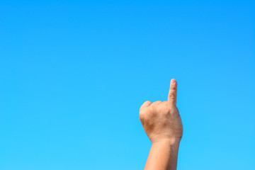 A male hand shows a small finger isolated against blue sky background.