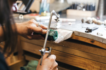 Cropped hands of female artisan cutting equipment with handsaw on table in workshop