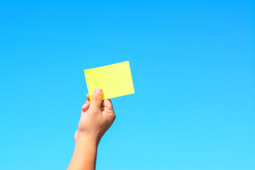 A male hand holds a green paper card with the blue sea as a background.