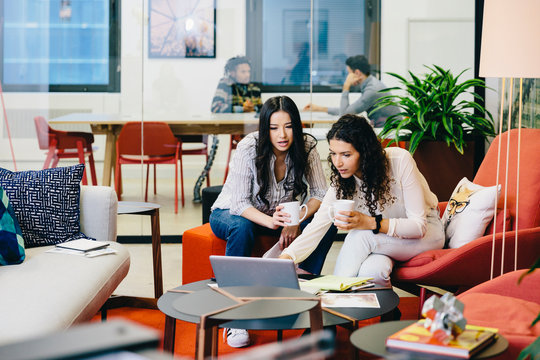 Businesswomen discussing over laptop computer while male colleagues planning in background at office