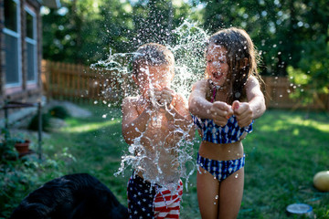 Cheerful siblings bursting water bombs while standing at backyard