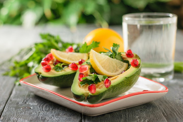 Avocado with pomegranate seeds, balsamic sauce, lemon and herbs and glass of water on the black table. Vegetarian cuisine for weight loss.