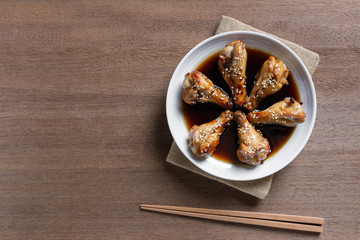 top view of grilled chicken drumette with teriyaki sauce in a ceramic dish on wooden table. asian homemade style food concept.