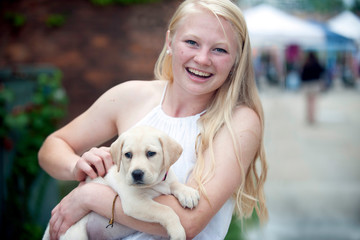 Portrait of cheerful young woman carrying puppy while standing in city