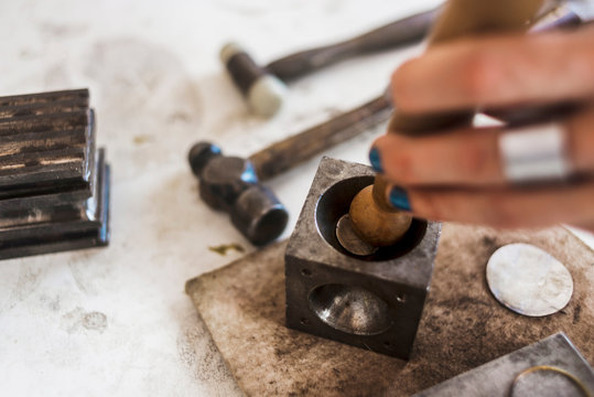 Cropped hands of female jeweller hammering dapping punch on doming block in workshop - Powered by Adobe