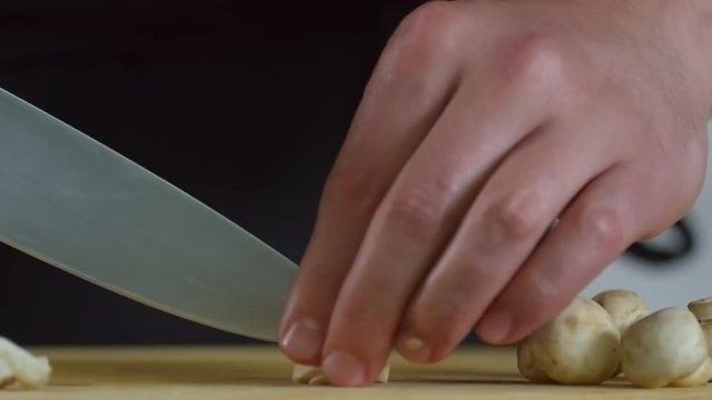 Close up shot of unrecognizable male cook cutting champignon mushrooms with sharp knife