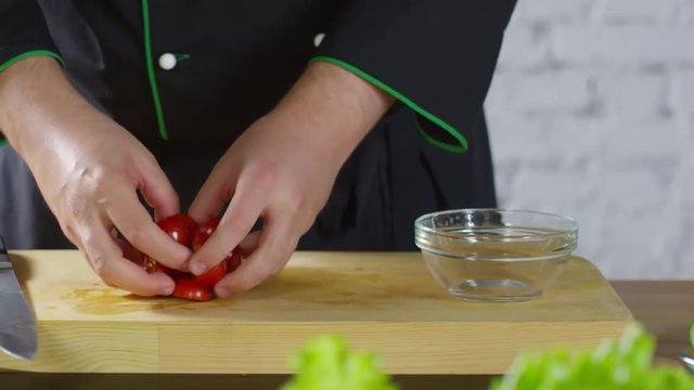 Mid-section tracking shot of unrecognizable male cook in uniform putting cut cherry tomatoes into glass bowl
