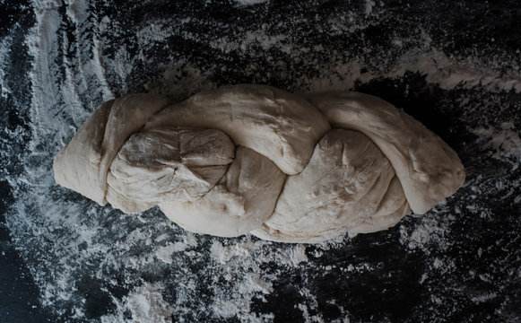 Overhead view of braided bread dough with flour on table at home