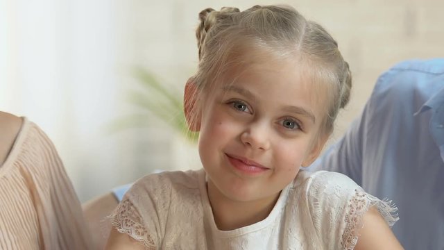 Caring parents tenderly kissing on cheeks their little daughter, love and pride