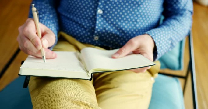 Casual Businessman Sitting On Chair And Writing Notes In A Journal