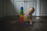 Portrait of girl with colorful toys sitting on hardwood floor at home