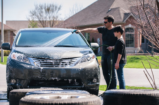 Father washing car while standing by son on driveway
