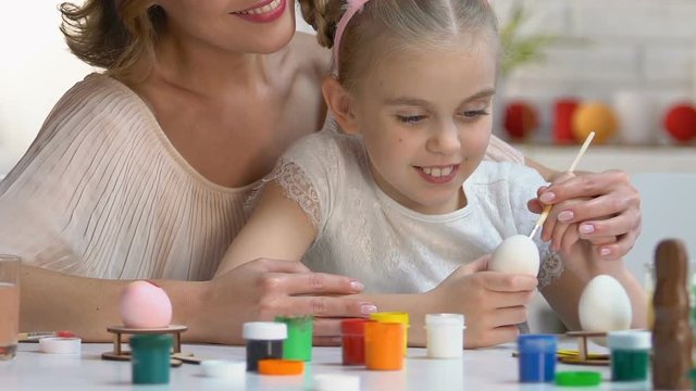 Loving mother teaching left-handed daughter to decorate Easter eggs with paint