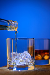 Whiskey is poured in a glass with ice on a blue background
