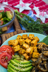 Buddha bowl for Christmas lunch, dinner. Fried tofu, avocado slices, mushrooms, tomatoes, spinach. Healthy vegetarian food. Red tablecloth.