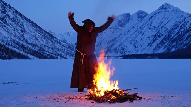 Happy fat fire-worshipper monk dancing on lake ice near the fire in winter