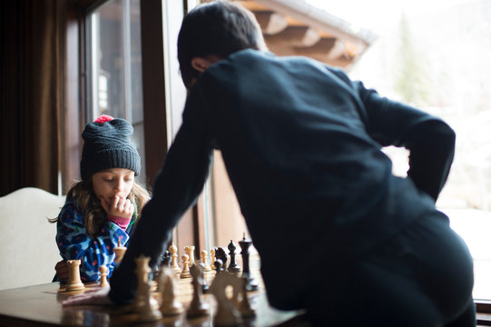 Siblings playing chess while standing by window at home