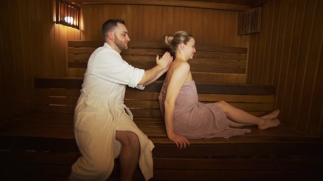 A man makes a back and neck massage beautiful woman in the sauna, bath.