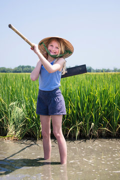 Portrait Of Girl With Work Tool Standing In Muddy Water On Farm