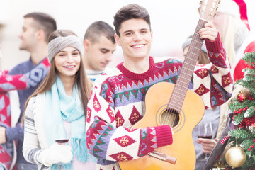 Young happy man with friends holding guitar on balcony on Christmas