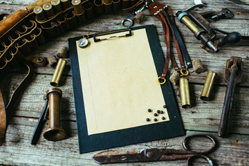 Set of hunting equipment on vintage desk. Hunting belt with cartridges, and clipboard with paper on old wooden background. Top view