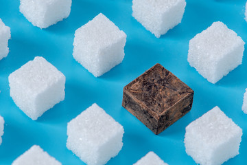 Pattern of sugar refined cubes and one chocolate blue background. Concept of harmful ingredient for confectionery