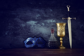 low key image of wine cup, mysterious mask and sword. fantasy medieval period.