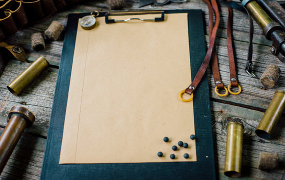 Closeup clipboard with paper on old wooden background. hunting equipment on vintage desk. Hunting belt with cartridges