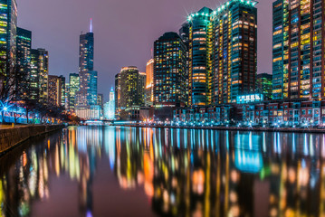 Illuminated modern buildings reflecting on calm Chicago River against sky at night