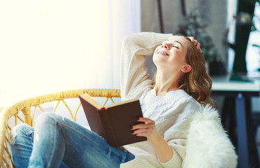 happy young woman reading a book by window