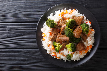 Portion of fried beef with broccoli with rice garnish and persimmon close-up on a plate. Horizontal...