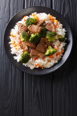 Portion of fried beef with broccoli with rice garnish and persimmon close-up on a plate. Vertical top view