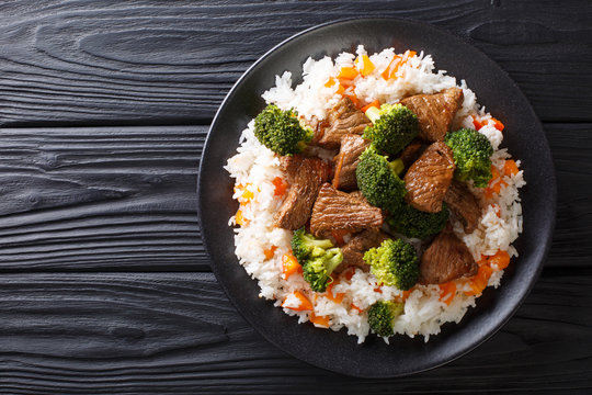 Portion of fried beef with broccoli with rice garnish and persimmon close-up on a plate. Horizontal top view