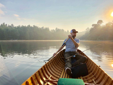 Man looking away while rowing boat on lake against sky during sunset