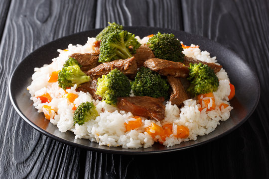 Portion of fried beef with broccoli with rice garnish and persimmon close-up on a plate. horizontal
