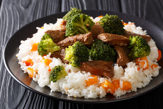 Asian beef with broccoli served with rice and persimmon close-up on a plate. horizontal