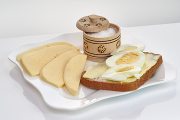 Sandwich with bread, butter, egg and cheese on a white plate and white background, close-up