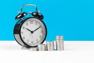 Alarm clock and money coins on the table.