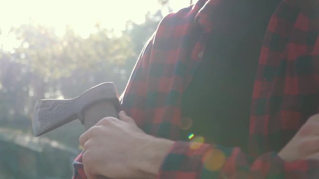 Bearded man with an ax in the sunlight outdoors. Brutal serious man stand near tree with axe in hand, thinking.