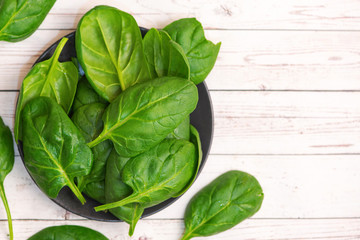 Fresh spinach leaves in bowl on light wooden table. Top view. With Copy Space