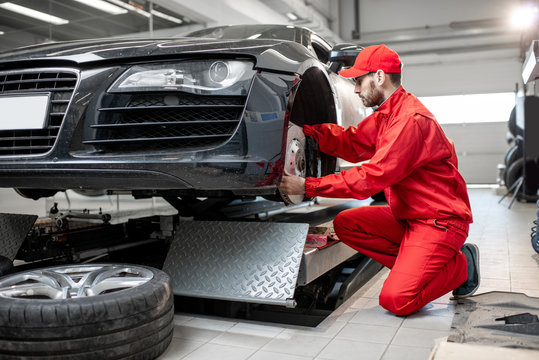 Auto Mechanic In Red Uniform Servicing Sports Car Checking Front Brakes In The Car Service