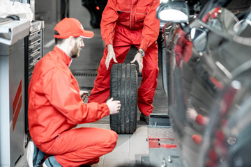 Fototapeta na wymiar Two car service workers in red uniform changing wheel of a sport car at the tire mounting service